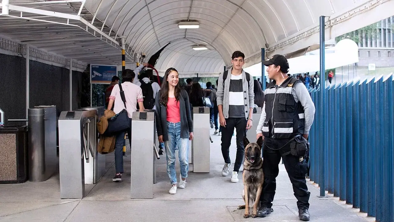Perro de trabajo, junto a un oficial de seguridad en la entrada de campus cuidando a los estudiantes del programa de estudios preparatoria sep