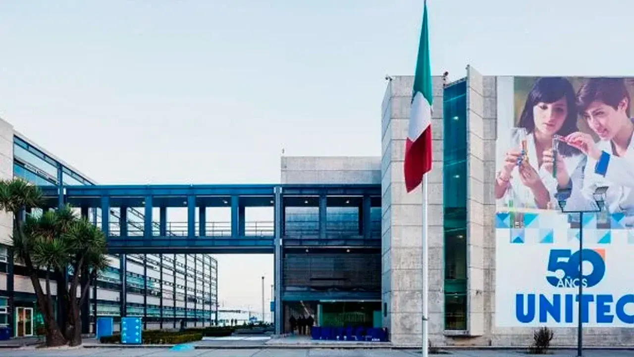 Un puente peatonal metálico conecta dos edificios modernos en un campus, creando un acceso entre ambos.