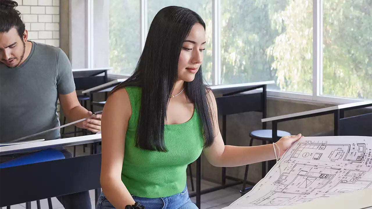 Estudiante de la carrera de arquitectura revisando un plano en el salón de clases