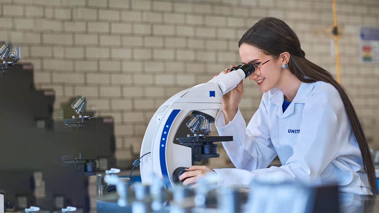 Alumna de la carrera de qfb de UNITEC utilizando un microscopio