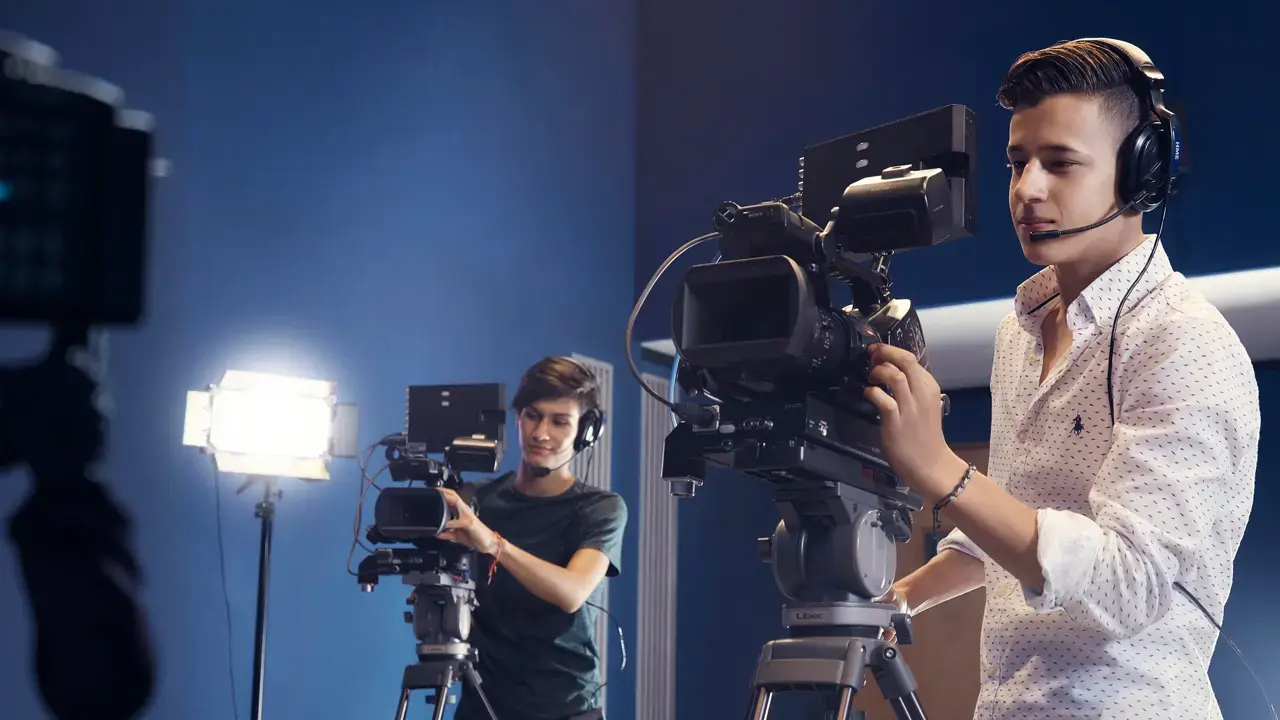 Dos alumnos de la carrera en publicidad manejando cámaras en el salón de TV durante una práctica