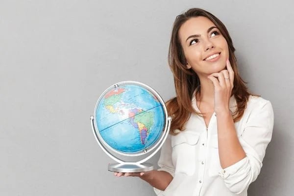 Una mujer sostiene un globo terráqueo, lo observa pensativa, frente a un fondo gris.