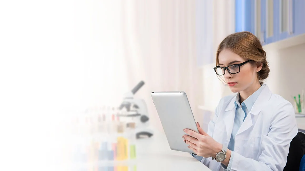 Estudiante de ing en química consultando información en iPad mientras realiza experimento.