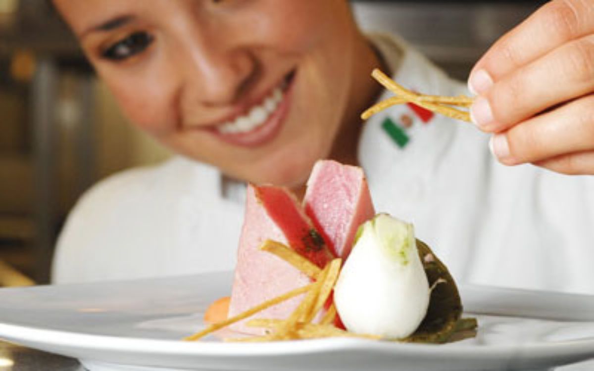 Chef sonriente decorando un platillo gourmet con ingredientes frescos en un restaurante profesional.