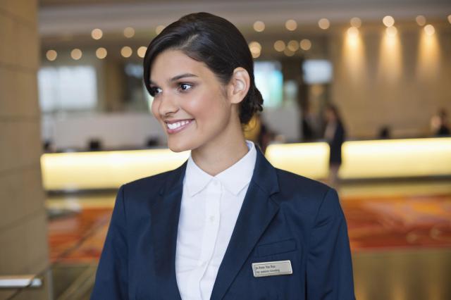 Recepcionista profesional con uniforme en un hotel, destacando la importancia de la atención al cliente en el sector turístico.