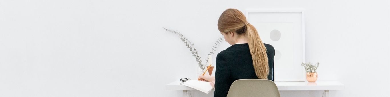 Mujer trabajando en un escritorio moderno, escribiendo en un cuaderno con enfoque en productividad y organización en el entorno laboral.